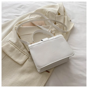 Close-up of white quilted crossbody bag with gold hardware on beige blazer background