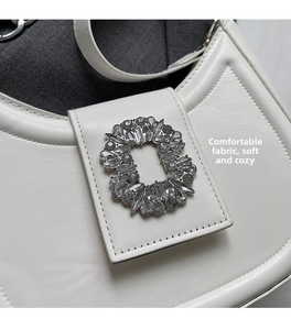 Détail d'un sac porté épaule en cuir blanc avec une boucle ovale ornée de cristaux