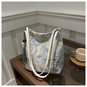 Détail du sac seau en jacquard bleu avec pompon gris et étiquette en cuir sur table