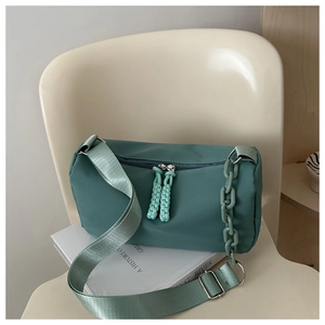 Detail of teal canvas crossbody bag with thick chain strap and woven zippers on a chair