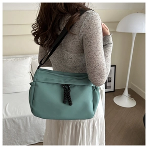 Detail of mint green nylon tote bag featuring black woven pullers and drawstring side pockets