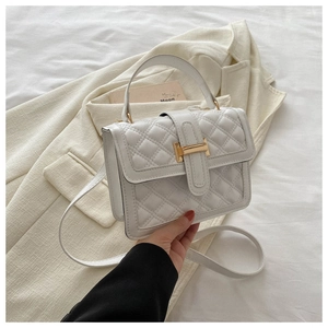 Detailed view of quilted faux leather handbag with gold H-shaped lock on a beige blazer