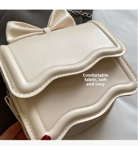 Detail of cream crossbody bag featuring wavy flap design and large leather bow decoration