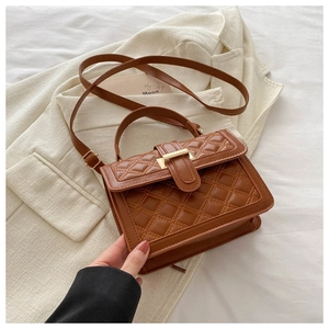 Detail of a brown quilted crossbody bag with gold metal buckle on a white blazer