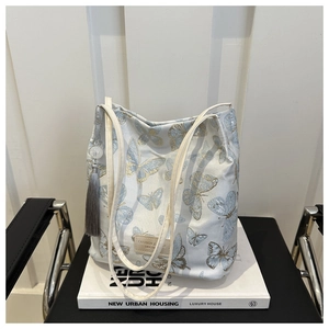 Détail du sac en tissu blanc avec broderie papillon et bandoulière en cuir sur un livre