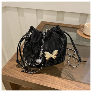 Detail of black pleated drawstring bucket bag with gold butterfly and metal chain strap