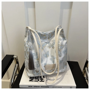 Détail de la broderie papillon bleue et du gland gris sur un sac cabas en toile