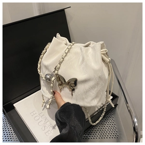 Detailed macro of white drawstring bucket bag with silver butterfly charm and chain strap