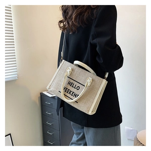 Close-up of beige canvas tote bag with Hello Weekend print worn by model in black blazer