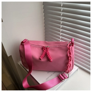 Detail of vibrant pink nylon crossbody bag with chunky chain decor and woven zipper pull