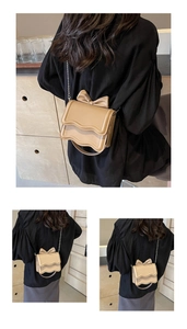 Detail view of wavy flap edge and 3D bow on beige crossbody bag with chain strap