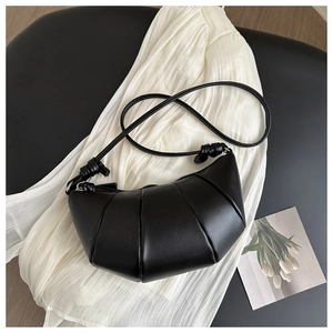 Détail du sac croissant plissé noir avec bandoulière nouée sur fond textile texturé