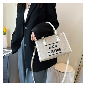 Model showing a cream canvas tote bag with HELLO WEEKEND print and white leather straps