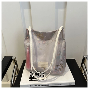 Détail du sac cabas en soie lavande avec broderie florale et pompon rose élégant