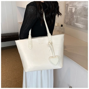 Close-up of a white tote bag with textured surface and a heart-shaped charm accessory