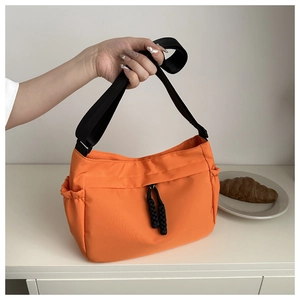 Detail of bright orange nylon crossbody tote with adjustable black strap and side pockets