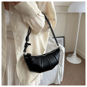 Detail of black pleated hobo bag with knotted shoulder strap worn by a model