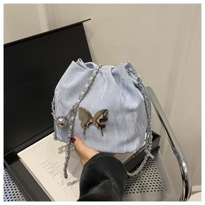 Détail du sac seau bleu clair avec texture froissée et grand ornement papillon en métal