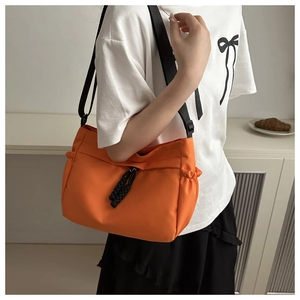 Detail of bright orange nylon tote bag with black wide strap shown on a model