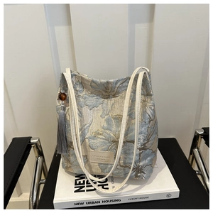 Détail d'un sac cabas en jacquard floral avec élégant long pompon et perles sur livre blanc