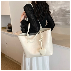 Side view of cream tote bag with textured finish and heart charm on a female model