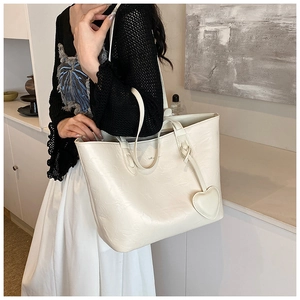 Detail of cream tote bag featuring floral embossing and a cute heart-shaped pendant