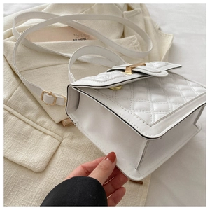 Detail of white quilted crossbody bag with golden metal lock on beige suit background