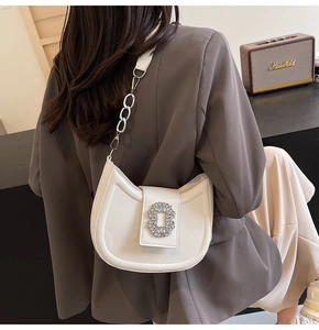 Close-up of a white saddle bag featuring a rectangular rhinestone buckle and chain strap