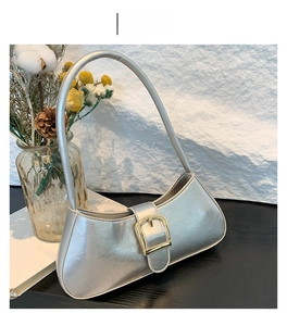 Detail of silver patent leather shoulder bag with textured finish and gold buckle