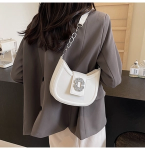Detail of white half-moon leather bag with rhinestone buckle and chain strap on shoulder