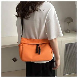 Rear view of bright orange nylon crossbody bag with black adjustable strap on a model