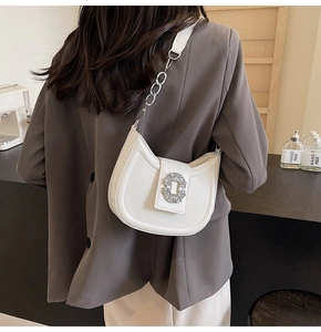 Close-up of white crescent bag with oversized rhinestone buckle and chain strap on model