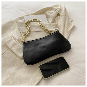 Détail d'un sac baguette noir avec chaîne dorée épaisse posé sur un blazer beige doux