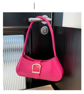 Detail of rose red patent leather bag with large gold buckle hanging on a door handle
