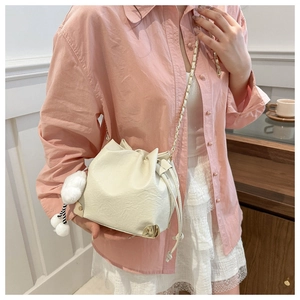 Detail of cream drawstring bucket bag with gold corners and plush charm on a model