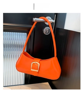 Detail view of vibrant orange leather baguette bag with signature gold buckle on handle