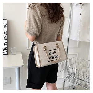 Detail of canvas tote bag with HELLO WEEKEND text and leather straps worn on shoulder