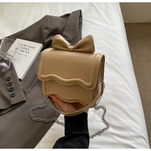 Detail of beige crossbody bag with large bow decoration and wave edge flap design