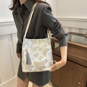 Sac bandoulière en toile beige avec broderie papillon bleu et élégant pendentif à franges