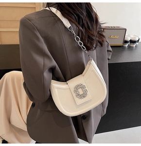 Detail of white crescent bag with crystal buckle and chain strap on shoulder
