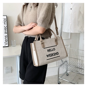 Detail of beige canvas tote bag with brown straps and Hello Weekend print
