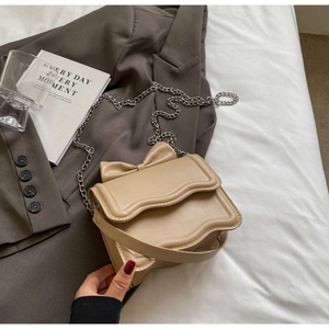 Detail of beige crossbody bag with bow decoration and wavy edges on a grey blazer