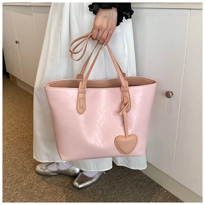 Close-up of pink tote bag with pleated texture and matching heart charm accessory