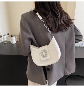 White crescent underarm bag featuring a sparkling rhinestone buckle and chain strap