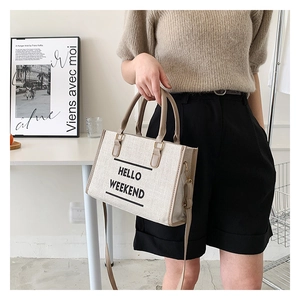 Detail of beige canvas tote with HELLO WEEKEND text, brown leather handles and shoulder strap