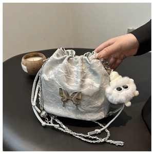 Detail of silver bucket bag with butterfly buckle, metal chain strap and plush monster charm