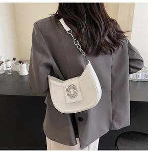 Close-up of a white hobo bag featuring a luxury rhinestone buckle and silver chain strap