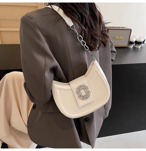 Chic beige crescent bag with crystal buckle shown on a model's shoulder in a cafe setting