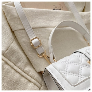 Detail of white quilted crossbody bag with golden metal buckle and fine stitching texture