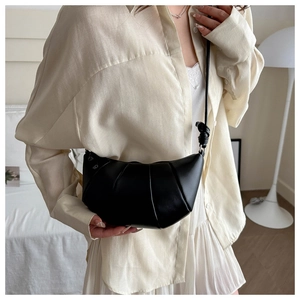 Détail d'un sac croissant noir au design plissé porté en bandoulière par un mannequin